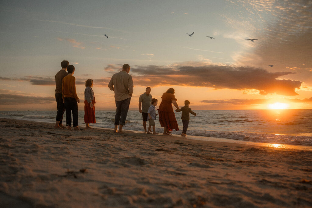 Extended family walking along Clearwater Beach at sunset, generations together as waves roll in and the sun sets over the Gulf.
